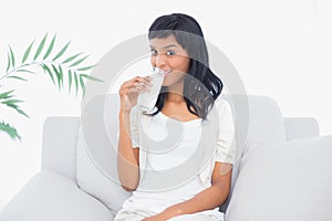 Charming black haired woman in white clothes drinking a glass of water