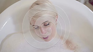 Charming blond Caucasian woman enjoying bath in the morning or in the evening. Top view portrait of smiling beautiful