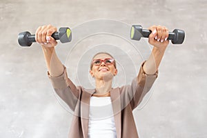 Charming blond woman holds dumbbells in hands in front of herself. Selective focus