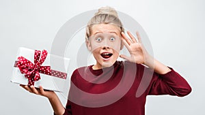 Charming blonde girl with gift posing with surprised face expression. Studio shot white background, isolated