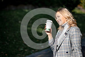 Charming blonde with long curly hair in gray-blue tweed jacket and matching cashmere sweater, holding cup of tea in her