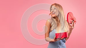 Charming blonde woman in lovely dress opening gift box in heart shape over pink studio background, banner design