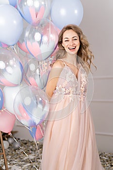 Charming blonde woman in stylish dress with bunch of birthday balloons over pink studio background, copy space. Party