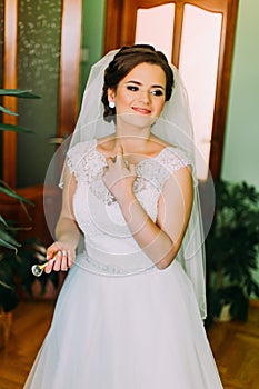 Charming bride in gorgeous white dress using perfume before wedding ceremony