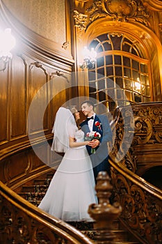 Charming bride and handsome elegant groom on old wooden stairs with the background of vintage interior