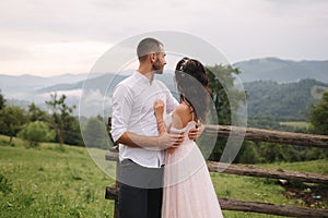 Charming bride hug her handsome groom in mountains. Beautiful wedding couple walk. Green gackground