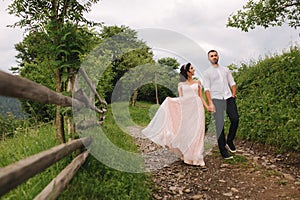 Charming bride hug her handsome groom in mountains. Beautiful wedding couple walk. Green gackground