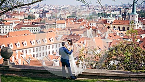 The charming bride is stroking the cheek of the groom at the background of the Prague panorama.