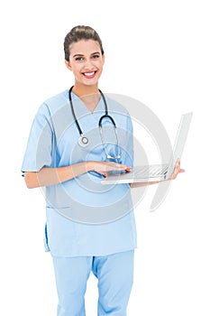 Charming brown haired nurse in blue scrubs using a laptop