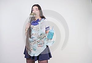 Charming brunette cooking girl in anime school uniform and kitchen apron on white background in Studio