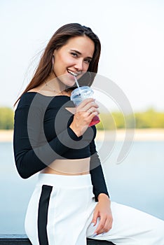 Charming brunette girl smiling and drinking cold drink summer outdoor. Young woman`s portrait. Female model posing over nature