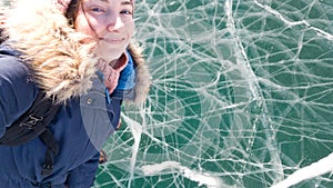 Charming brunette girl traveler takes a selfie standing on the clear bright ice of lake Baikal. Travel to Siberia.