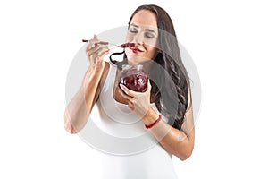 Charming brunette is holding a spoon sull of jam and smelling the tasty and sweet aroma. Isolated background photo