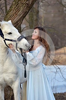 Charming brunette in pale blue dress with a white horse