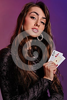 Brunette woman in black velvet dress showing two playing cards, posing against coloful background. Gambling