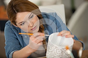 charming brunette woman paints clay cup