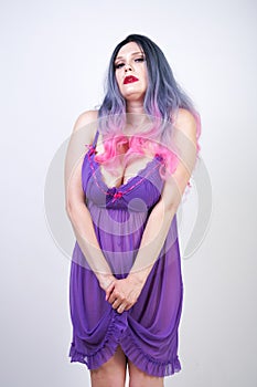 Charming buxom girl stands in a purple transparent nightgown lingerie on a white background in the Studio