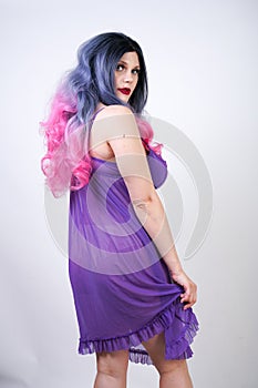 Charming buxom girl stands in a purple transparent nightgown lingerie on a white background in the Studio