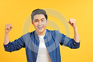 Charming casual man with hands up in the air while looking up victorious on yellow studio background