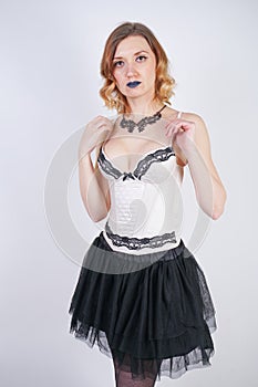 Charming caucasian blonde in lace beige lingerie bodice and black skirt on white background in Studio