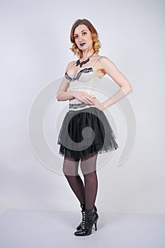 Charming caucasian blonde in lace beige lingerie bodice and black skirt on white background in Studio