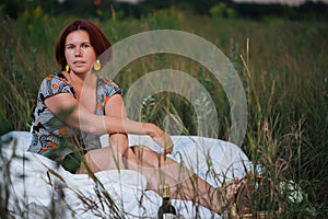 Charming caucasian woman 30-35 years old in the white bed in a field at sunset