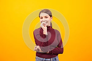Charming caucasian woman smiling and bitting her thumb over yellow background