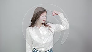 Charming caucasian young woman showing muscules, pointing with finger on it.