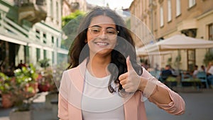 Charming cheerful young Indian Arabian ethnic woman girl female businesswoman positive showing thumb up outside city