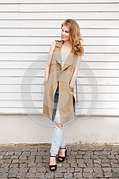 Charming cheerful young woman in a light summer vest in a stylish T-shirt in blue ripped jeans in black shoes with high heels