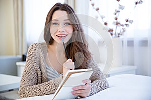 Charming cheerful young woman thinking and writing in notepad