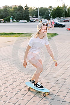 Charming and cheerfull girl longboarding in the park, she is wearing light pink shorts photo