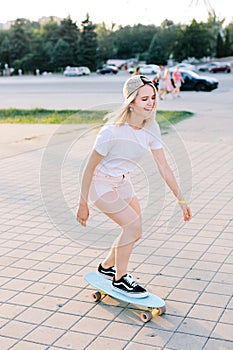 Charming and cheerfull girl is scateboarding in the park, she is wearing light pink shorts photo