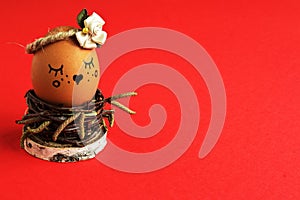 Charming coquettish light brown egg with satin flower in pastel ton in homemade wicker of birch twigs in nest on red background.