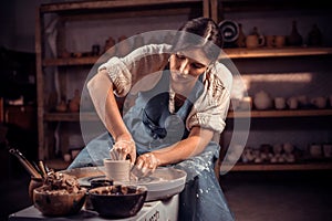 Charming craftsman works with clay on a potter`s wheel. The concept of craft creativity.