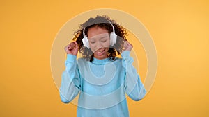 Charming curly african american woman she listens to music with headphones closing her eyes. isolated yellow background