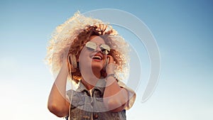 Charming curly blonde listen to music. Young woman with big headphones. outdoors portrait of a trendy girl