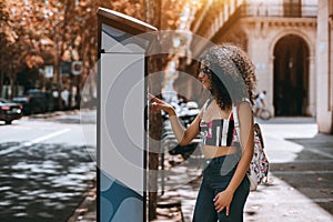 Charming curly girl is paying parking meter outdoors