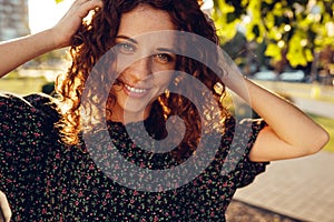 Charming curly red-haired girl with freckles in dress poses for the camera in the city center showing different facial emotions