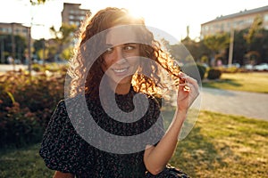 Charming curly red-haired girl with freckles in dress poses for the camera in the city center showing different facial emotions