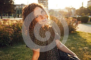Charming curly red-haired girl with freckles in dress poses for the camera in the city center showing different facial emotions