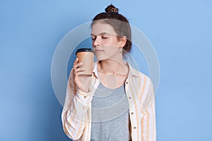 Charming cute casual dark haired pretty fascinating girl smelling her tea or coffee in paper cup, wearing casual shirts isolated