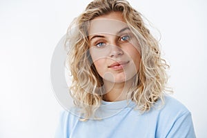 Charming and cute sincere blonde woman with short curly hairstyle and blue eyes in t-shirt tilting head intrigued