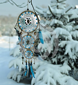 Charming dreamcatcher with owl decoration agains snow landscape and conifer.