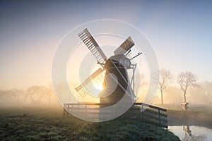 Charming Dutch windmill in fog at dawn