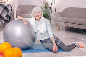 Charming elderly woman posing near exercise ball