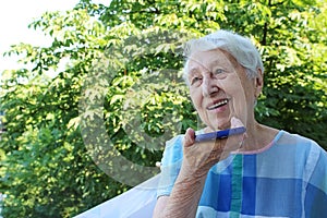 Charming elderly woman in rectangular black rimmed eyewear using voice recognition function on cell phone.