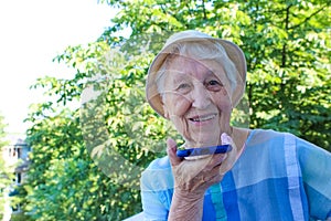 Charming elderly woman in rectangular black rimmed eyewear using voice recognition function on cell phone.