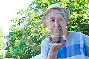 Charming elderly woman in rectangular black rimmed eyewear using voice recognition function on cell phone.