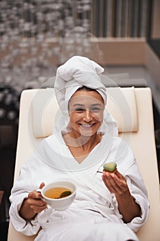 Charming elegant Caucasian woman holding cup of tea and green cake i hands while looking at the photo camera in wellness